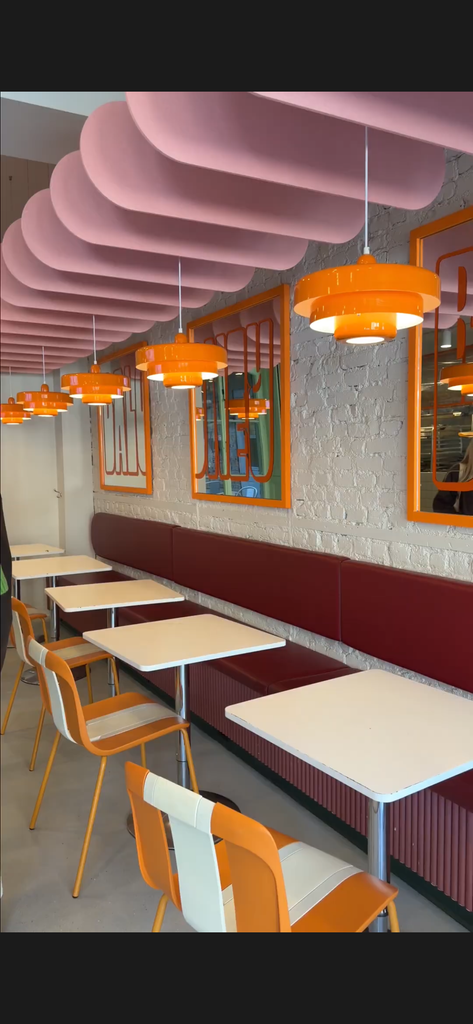 Intérieur du Saint-Jean Comédie Club à Québec, avec banquettes bourgogne, chaises orange, luminaires colorés et décor contemporain pour une ambiance conviviale.