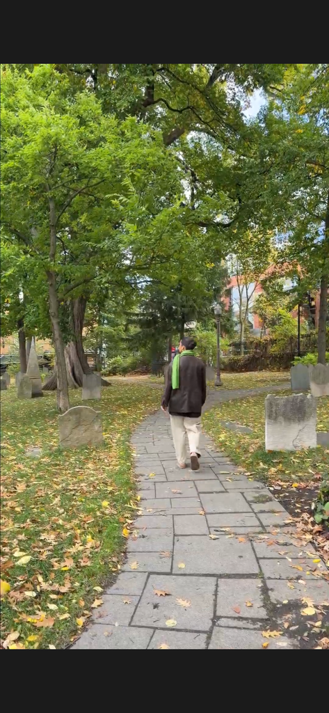 Une personne se promène parmi les pierres tombales du cimetière Saint-Matthew à Québec, sur un sentier bordé d’arbres et de feuilles d’automne.